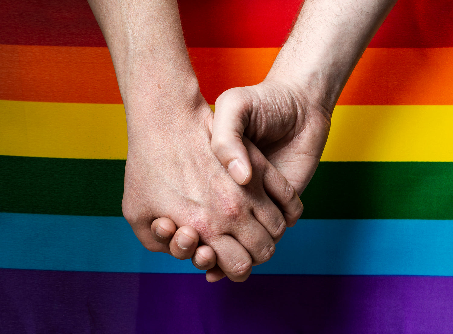 Two men holdings hands on top of a gay pride flag